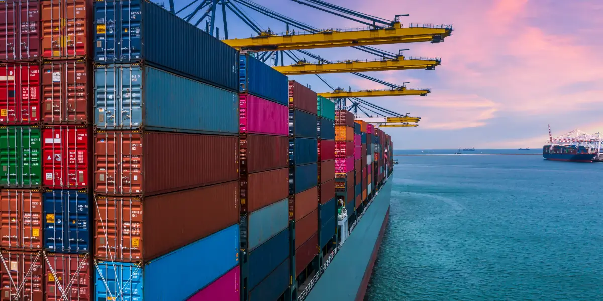 Beladenes Containerschiff am Terminal rosa-roter Himmel und blaugrünes Wasser