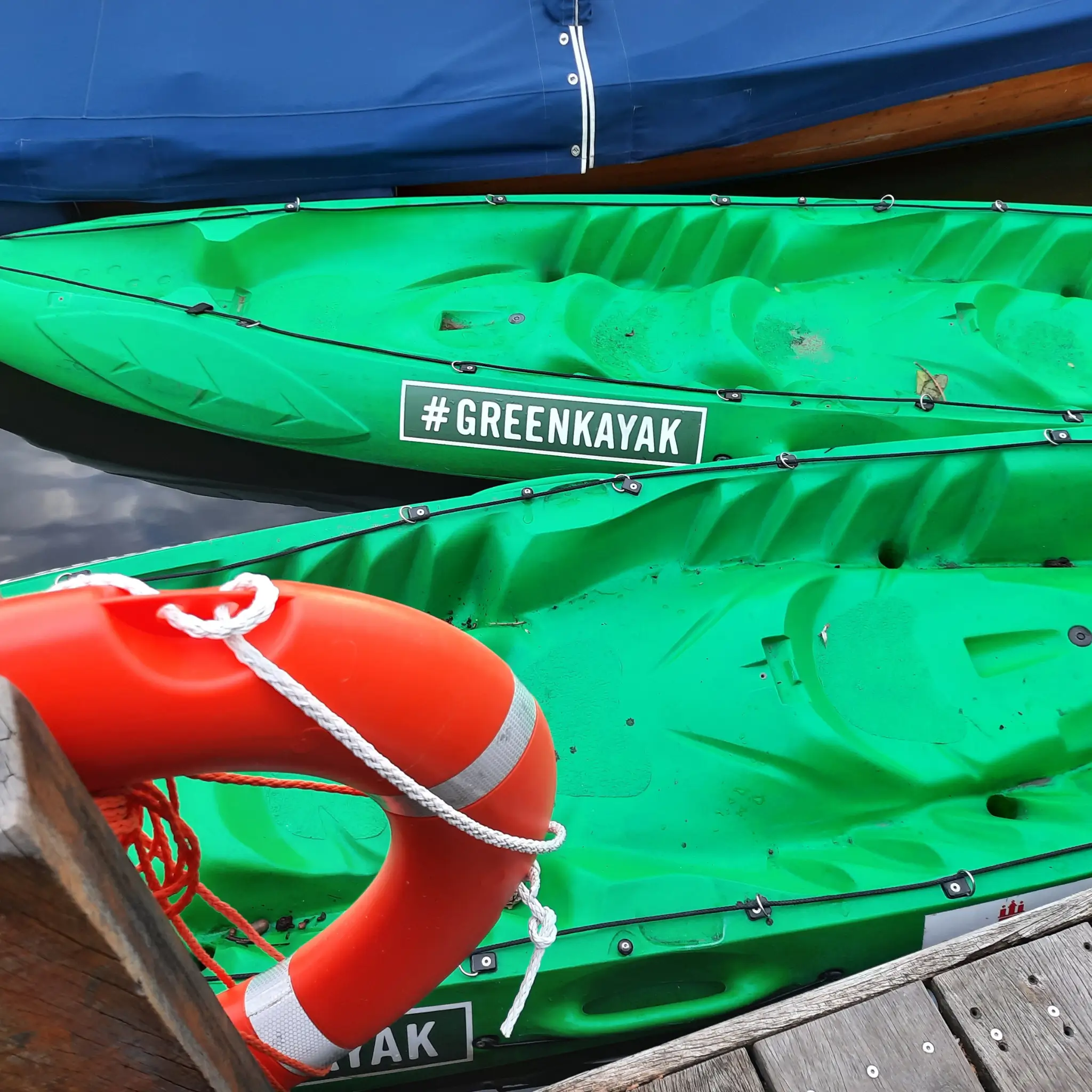 Zwei grüne Kayaks im Wasser, Rettungsring am Steg