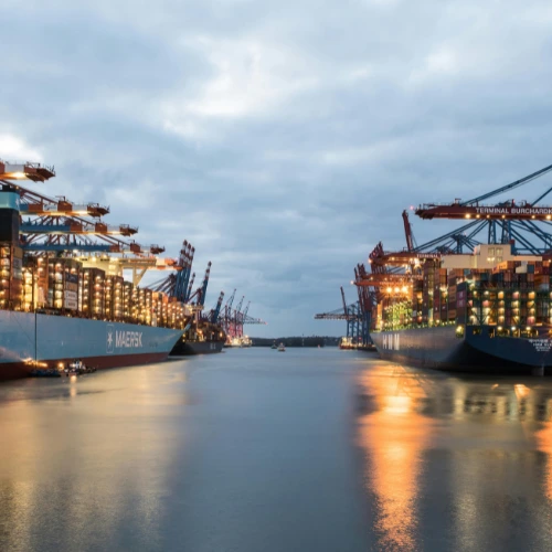 Zwei beladene, beleuchtete Containerschiffe am Containerterminal